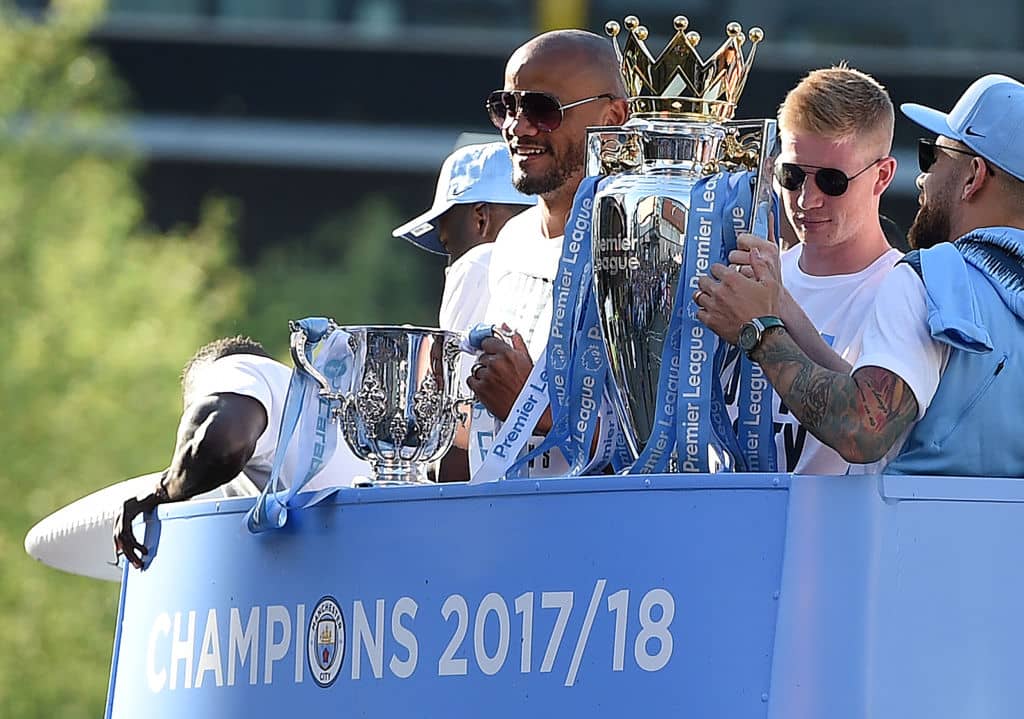 Manchester City's Belgian midfielder Kevin De Bruyne (2R) holds up the Preimer Leagu trophy as Manchester City's Belgian defender Vincent Kompany (C) holds up the English League Cup trophy to fans as the Manchester City team take part in an open-top bus parade through Manchester, northern England on May 14, 2018 to celebrate winning the 2018 Premier League title. - Manchester City set the seal on a record-breaking season by becoming the first side in English top flight history to hit 100 points with victory at Southampton on Sunday. City also added another landmark by winning the league by a record 19 points from local rivals Manchester United. (Photo by Oli SCARFF / AFP) (Photo credit should read OLI SCARFF/AFP/Getty Images)